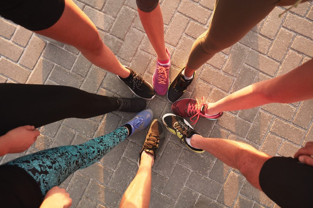 Built By She. Legs of athletes wearing sports shoes in a circle. Top view of runners standing together.