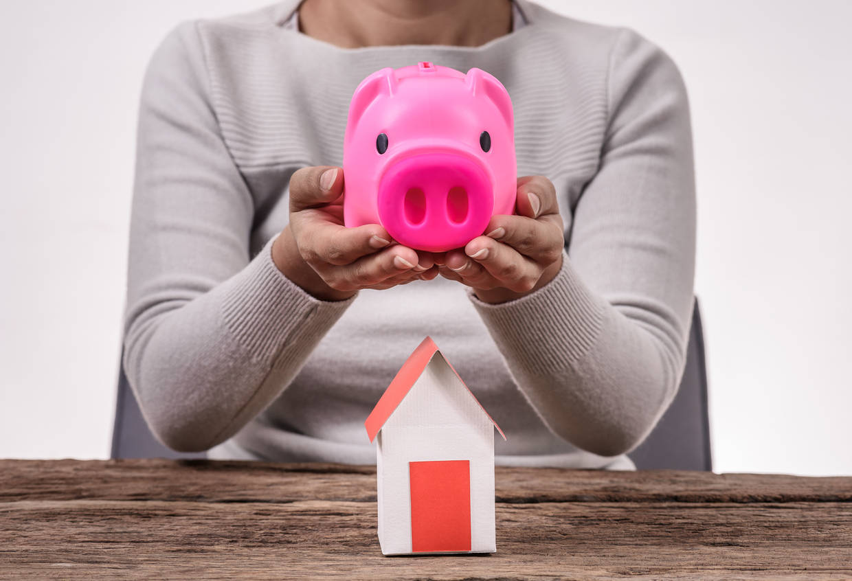 Built By She - Woman holding piggy bank and model million dollar home