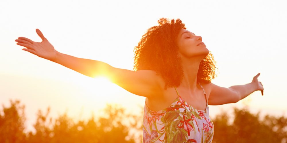 Built By She- Avocado Beautiful mixed race woman expressing freedom on a summer evening outdoors with her arms outstretched