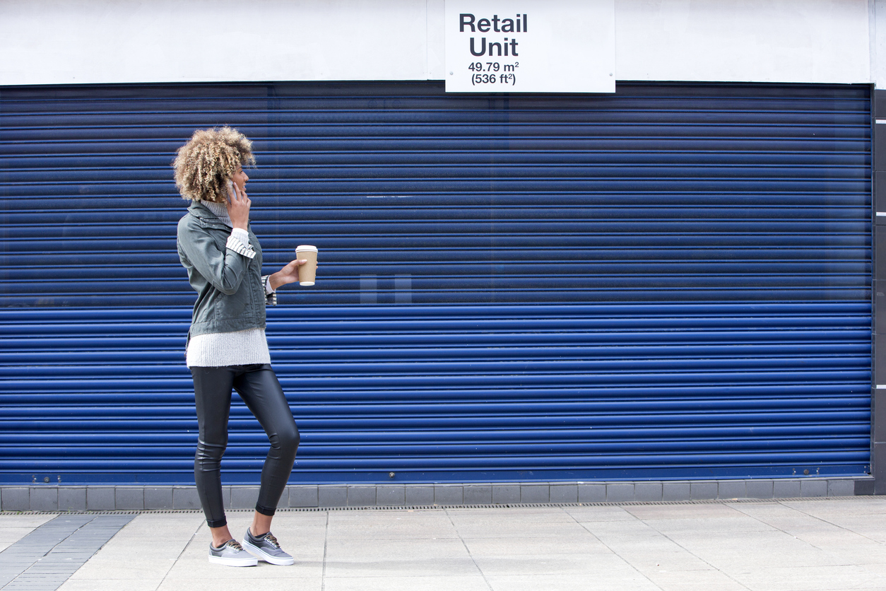 Built by She - Young woman enquiring about a retail unit on the phone. She is dressed casually and is holding a disposable coffee cup.