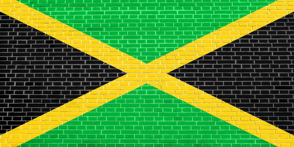 Built By She - Flag of Jamaica on brick wall texture background